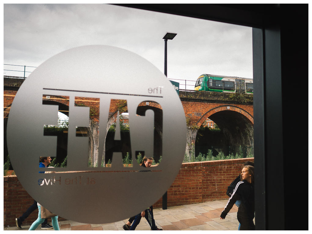 In The Hive
The Cafe at The Hive, Worcester...a group of passers by head away from the river and on towards the town.  On the arches above a London Midland Class 170 approaches Worcester Foregate Street with 1M67 1339 Hereford to Birmingham New Street.
