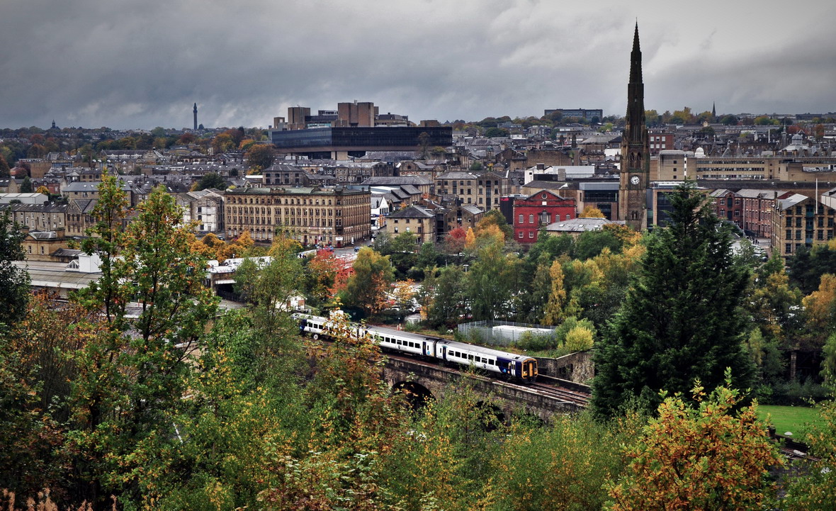 A Little X-tra from Halifax
Notwithstanding the slightly altered tag line from an old TV advert, there is plenty of interest in the Halifax skyline here, as a Northern class 158 DMU leaves the station and crosses Beacon Hill viaduct with a Huddersfield to Bradford Interchange service on 23rd October 2022. The modern building with the dark glass exterior, which stands out a bit like a sore thumb, is in fact the Halifax head office of the Lloyds Banking Group and Halifax Building Society.
