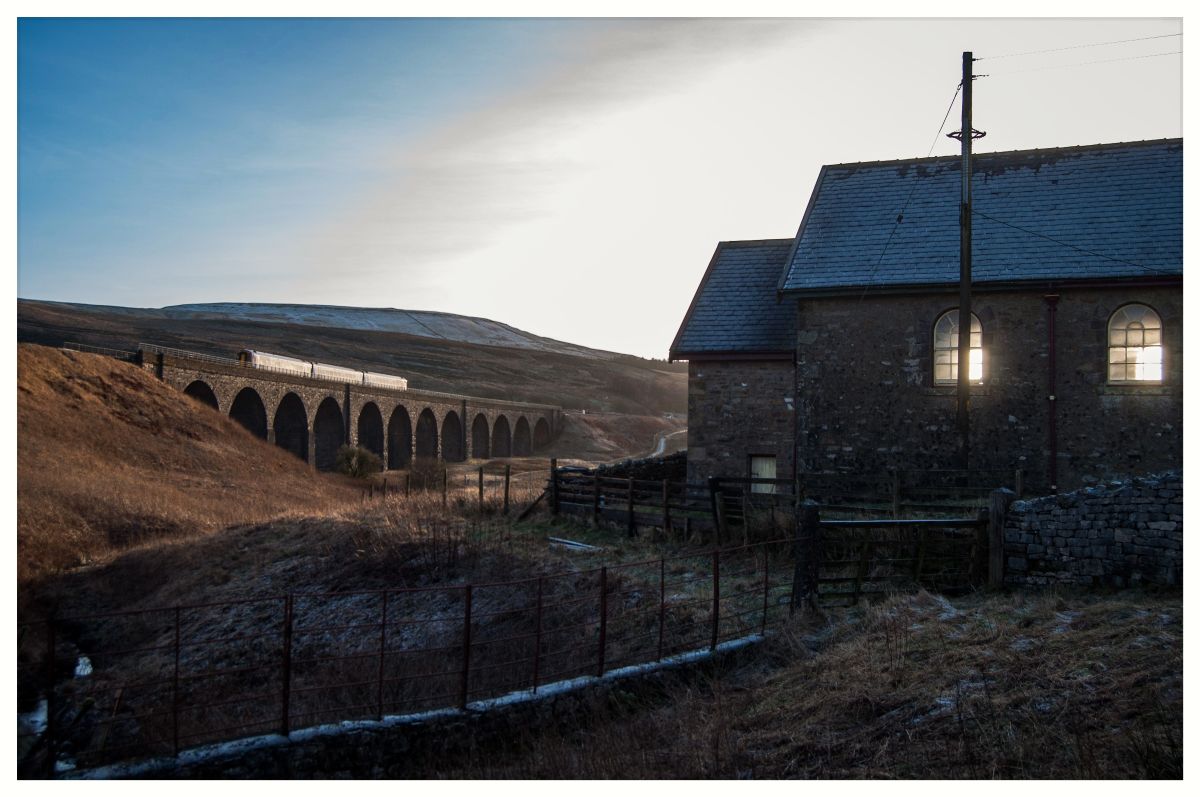 Winter Glow
Whilst out photographing around Garsdale on a crisp and chilly day, I was attracted to this scene featuring the old Methodist chapel, and the way in which the sun was shining through the windows, making them glow. In the background, a Northern 158 crosses Dandry Mire Viaduct with the mid-afternoon Leeds to Carlisle service.
Keywords: SettleCarlisle;GarsdaleHead;HawesJunction;MethodistChapel;Northern