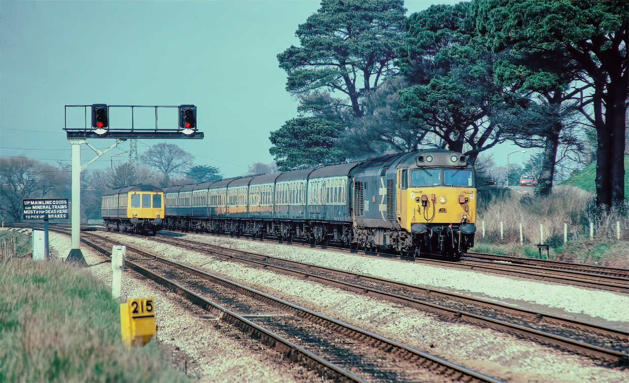 Bow and Aller...
I have just given this old shot a bit of a make over in the virtual darkroom. It has had some dust and scratch removal, a little sharpening and a run through Topaz DeNoise.  
It is a shot that can't be recreated in any way shape or form and shows 50012 Benbow running a rake of Mk 1s on a Newton Abbot to Paignton service which would then form the 1425 Paignton to Paddington. 
The road behind Benbow has now been upgraded to a dual carriageway and a big white wall separates the road from the railway. Behind the DMU is a Sainsburys superstore. The trees have gone and so has that amazing "Pick up brakes" sign. Aller Junction is a few hundred yards behind be.
