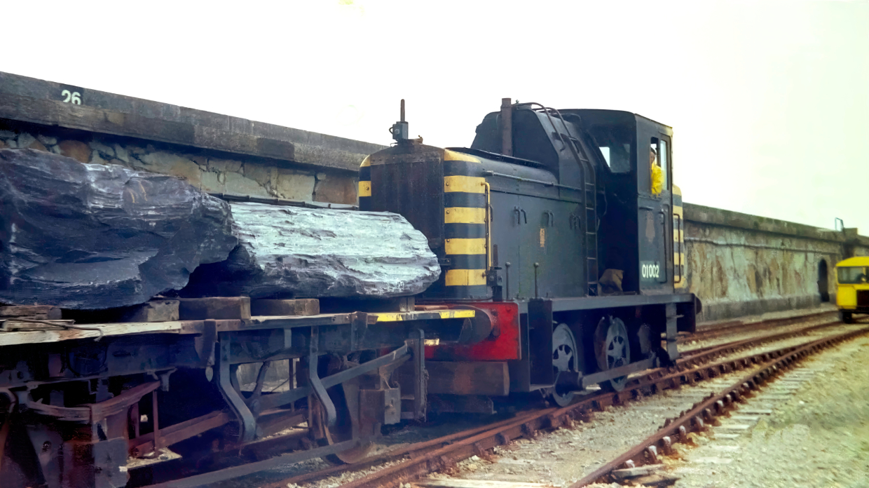 Break Out
01002 is seen hauling a typical load for the class of boulders which were used to reinforce the breakwater. The shunter was supposed to be in black livery but I never really could tell if it was just very dirty green. 01001 seldom ventured out of its shed and from 79 was used for spares. 01002 was cut up on site in March 81.
